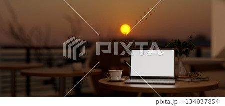 White screen laptop and coffee cup on wooden stool table at cafe's rooftop or balcony in the evening 134037854