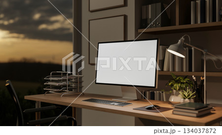 White screen computer on wooden table with books and potted plants under lamp light in study room. 134037872