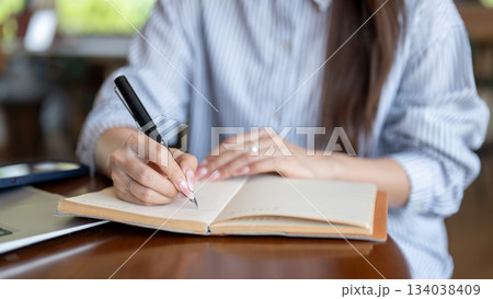 Close up of blue shirt woman writing in notebook by fountain pen while sitting at cafe wooden table 134038409
