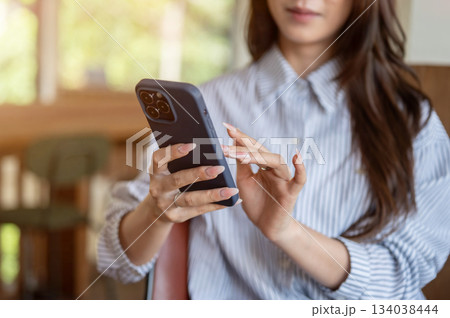 Close up of woman in blue shirt looking and typing on her phone while sitting on cafe's wooden chair Close up of woman in blue shirt looking and typing on her phone while sitting on cafe's wooden chair 134038444
