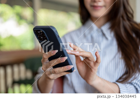 Close up of a long nails woman in blue shirt looking and typing on her phone while sitting in the cafe. Close up of a long nails woman in blue shirt looking and typing on her phone while sitting in the cafe. 134038445
