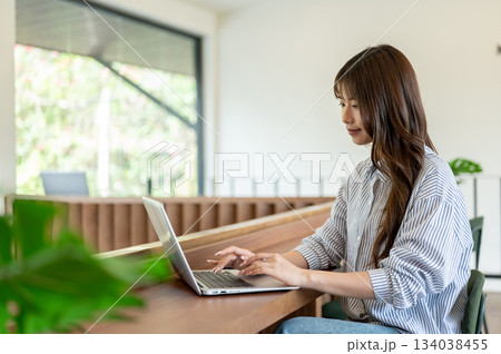 Smiling asian woman typing on laptop with both hand sitting at wooden counter in cafe or library. Smiling asian woman typing on laptop with both hand sitting at wooden counter in cafe or library. 134038455