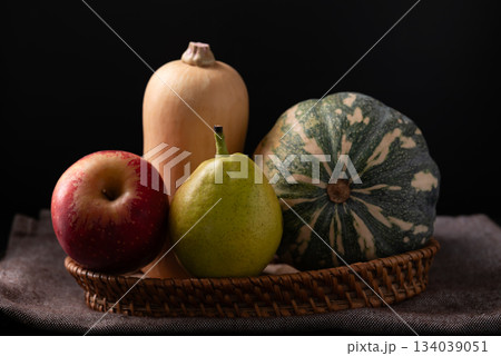Red apple, pear and butternut squash in basket on fabric with black background Red apple, pear and butternut squash in basket on fabric with black background 134039051