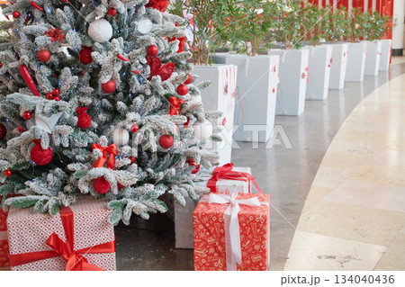 Flocked christmas tree decorated with red and white ornaments, presents underneath in shopping center 134040436