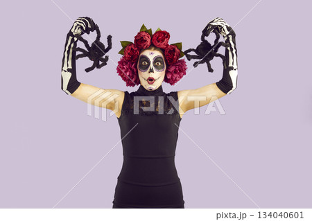 Woman in spooky Halloween costume holding toy spiders and making funny surprised face 134040601