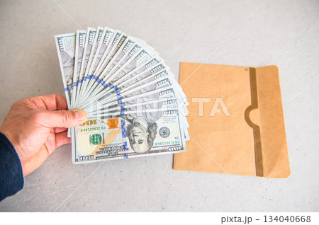 米100ドル紙幣17枚を左手で扇状に広げ左側から差し出す封筒と並べたアングルショット 米100ドル紙幣17枚を左手で扇状に広げ左側から差し出す封筒と並べたアングルショット 134040668