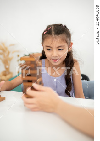 Asian kid or a girl in purple shirt playing a wooden tower building game with parent at white table 134041869
