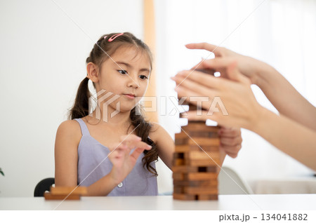 Asian kid girl in purple shirt looking at her parent hand while playing a wooden tower game together 134041882