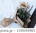 Top down winter scene of fir tree wrapped in kraft paper beside a mesh bag of oranges on snowy ground.  134044965