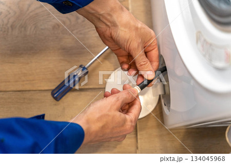 A home appliance repairman checks the filter blockage of a home washing machine A home appliance repairman checks the filter blockage of a home washing machine 134045968