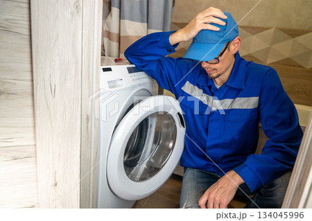 A home appliance repairman has difficulty repairing a home washing machine 134045996