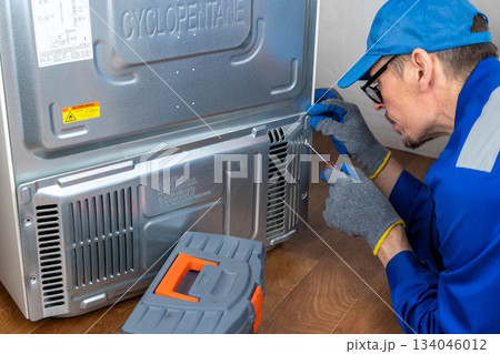 Repairing a refrigerator at home by a technician with blue gloves and tools Repairing a refrigerator at home by a technician with blue gloves and tools 134046012