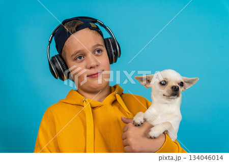 Young boy wearing headphones holds small dog against blue background 134046014