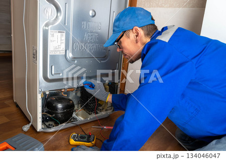 Repair work on refrigerator unit in home kitchen during afternoon hours Repair work on refrigerator unit in home kitchen during afternoon hours 134046047