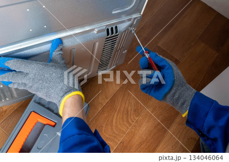 Person repairs kitchen appliance with screwdriver while wearing gloves in home Person repairs kitchen appliance with screwdriver while wearing gloves in home 134046064