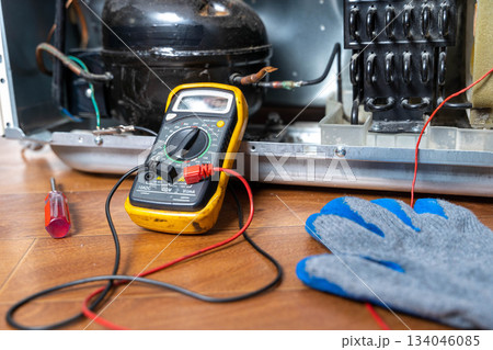 Repair technician checks electrical connections inside refrigerator on a workbench 134046085