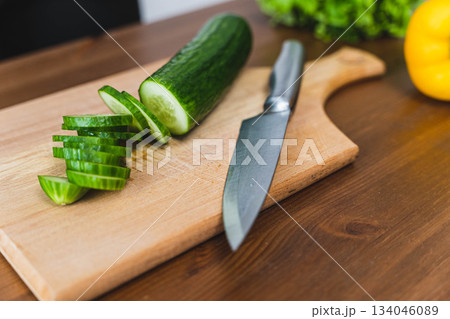 Slicing cucumber on wooden cutting board during kitchen meal preparation 134046089