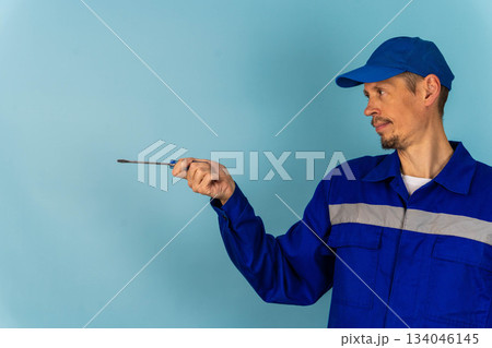 Man in blue uniform holding tool points to empty wall in workshop setting 134046145
