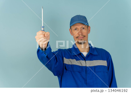 Man holds screwdriver in workshop environment during daytime with blue background Man holds screwdriver in workshop environment during daytime with blue background 134046192