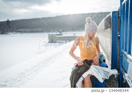 Senior woman getting dressed after swimming in an icy lake for health benefits. Senior woman getting dressed after swimming in an icy lake for health benefits. 134046344