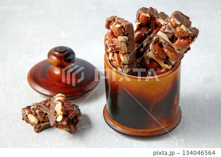 Photo of sweet chocolate bars with nuts in a wooden jar on a gray background. Photo of sweet chocolate bars with nuts in a wooden jar on a gray background. 134046564