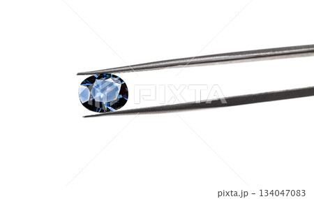 A blue gemstone is being held up by a jeweler's loupe A blue gemstone is being held up by a jeweler's loupe 134047083