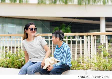 Mother and child enjoy summer day in city, family woman smiling with son on urban street, parent and people bond happily sharing conversation during outdoor leisure in modern architecture setting. Mother and child enjoy summer day in city, family woman smiling with son on urban street, parent and people bond happily sharing conversation during outdoor leisure in modern architecture setting. 134047560