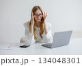 Frustrated woman in glasses working on laptop surrounded by paperwork at a bright office 134048301