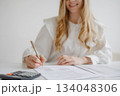 Person reviewing documents with a calculator on a desk during a work session in a bright office setting 134048306