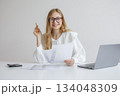 Professional woman in a white blouse working with documents and laptop while smiling at the camera 134048309