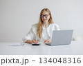 Young woman working on laptop with calculator during daytime in a minimalistic workspace 134048316