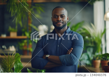 Confident man in blue shirt stands among lush greenery in a modern indoor setting during bright daylight Confident man in blue shirt stands among lush greenery in a modern indoor setting during bright daylight 134048376