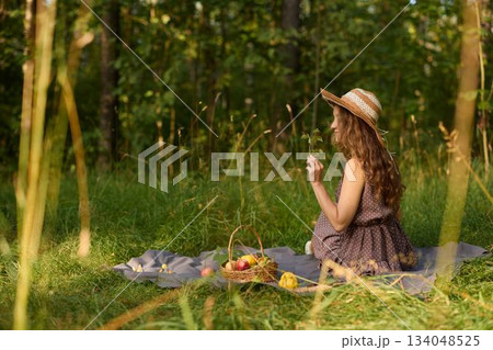Elegant female posing amid trees and grasses holding fruit in casual style 134048525