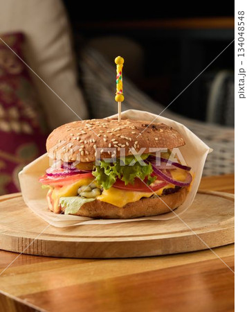 Sophisticated cheeseburger served on wooden platter featuring vibrant produce and melted cheese Sophisticated cheeseburger served on wooden platter featuring vibrant produce and melted cheese 134048548