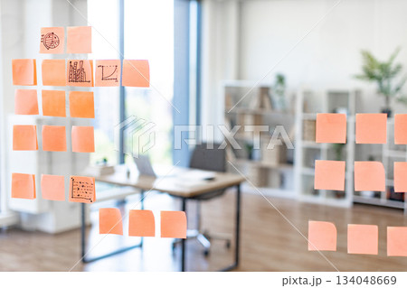 Sticky notes with charts and graphs are displayed on a glass wall in a modern office setting Sticky notes with charts and graphs are displayed on a glass wall in a modern office setting 134048669