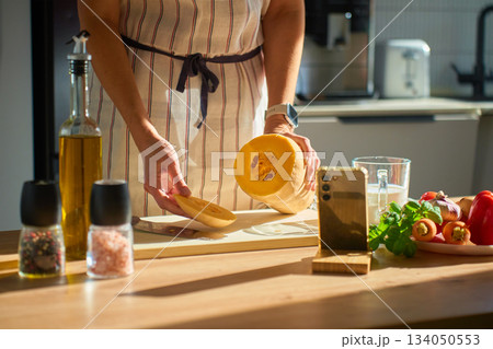 Woman slicing pumpkin on cutting board in kitchen 134050553