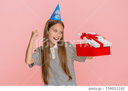Child girl jumps with joy waves hands celebrating birthday while happily receiving surprise gift box Child girl jumps with joy waves hands celebrating birthday while happily receiving surprise gift box 134051192