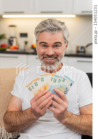 Middle-aged man counts money cash euros smiles at big plans purchase salary bonus savings investment 134051231