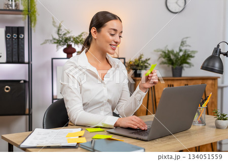 Young businesswoman opens laptop lays stickers and starts first task from list with confident focus Young businesswoman opens laptop lays stickers and starts first task from list with confident focus 134051559