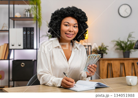African American businesswoman counts dollar cash notes family budget writes expenses on notebook 134051988