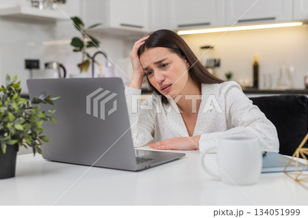 Young woman looks sad at laptop bad news lost game rejected project nervous clicks frown dark mood 134051999