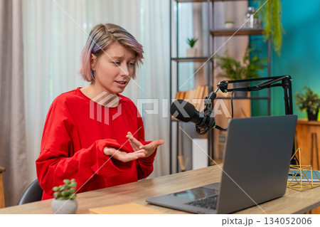 Young confident woman recording video interview at laptop speaking seriously in studio microphone 134052006