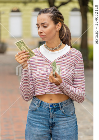 Poor young woman on city street holding one dollar banknotes lack of money to buy purchase something 134052119