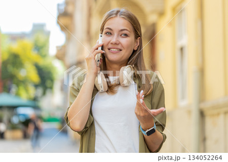 Happy Caucasian young woman tourist in pleasant conversation on smartphone standing on city street Happy Caucasian young woman tourist in pleasant conversation on smartphone standing on city street 134052264