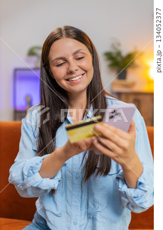 Happy young woman doing payments online purchase shopping in internet store holding bank credit card Happy young woman doing payments online purchase shopping in internet store holding bank credit card 134052377