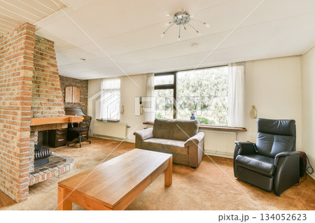 Modern living room featuring a brick fireplace, comfortable seating, and large windows that invite natural light, creating a warm and inviting atmosphere. 134052623