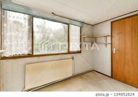 An uncluttered room showcasing large windows that allow ample natural light to fill the space, accompanied by a wooden door and a shelf. 134052624