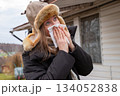 Caucasian woman in winter clothes sneezes into a white paper napkin outside. Virus, runny nose, illness, high body temperature, allergy 134052838