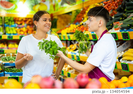 Friendly guy seller helps a girl buyer choose a fresh greenery 134054594