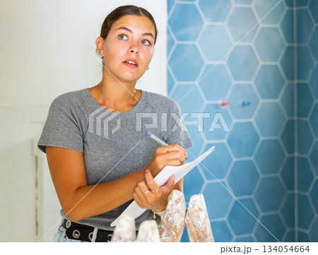 Young woman makes notes on paper while standing in the bathroom 134054664